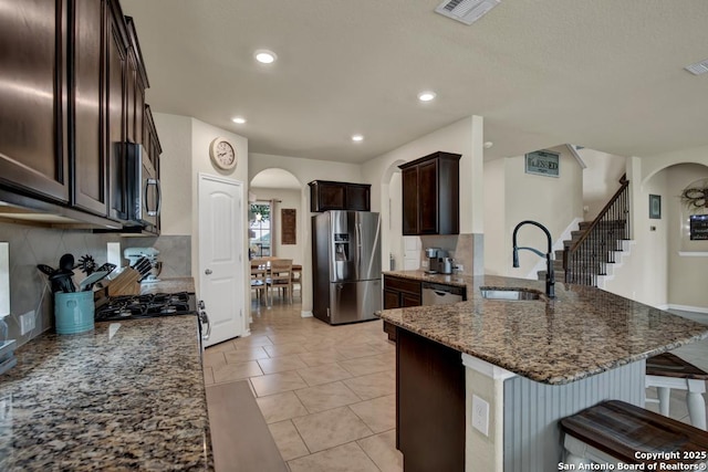 kitchen with arched walkways, a sink, visible vents, appliances with stainless steel finishes, and dark stone counters