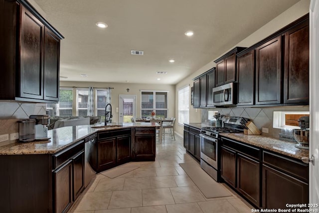 kitchen featuring light stone counters, visible vents, stainless steel appliances, and a sink