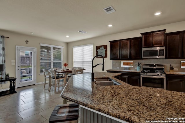 kitchen with dark brown cabinetry, visible vents, appliances with stainless steel finishes, light stone countertops, and a sink