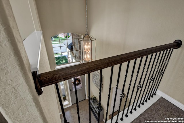 stairway featuring baseboards, tile patterned floors, a towering ceiling, and an inviting chandelier