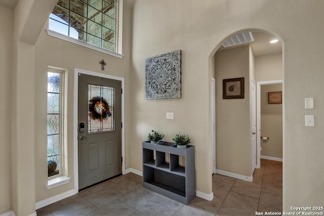 foyer entrance with arched walkways, light tile patterned floors, a high ceiling, visible vents, and baseboards