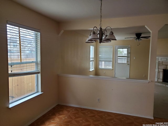 unfurnished dining area with a fireplace, baseboards, and ceiling fan with notable chandelier