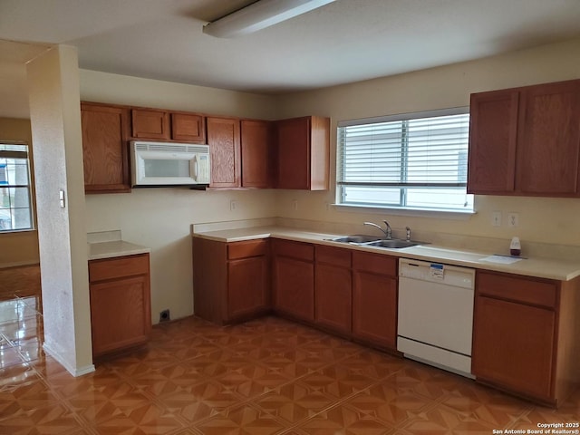 kitchen featuring white appliances, brown cabinets, a sink, and light countertops