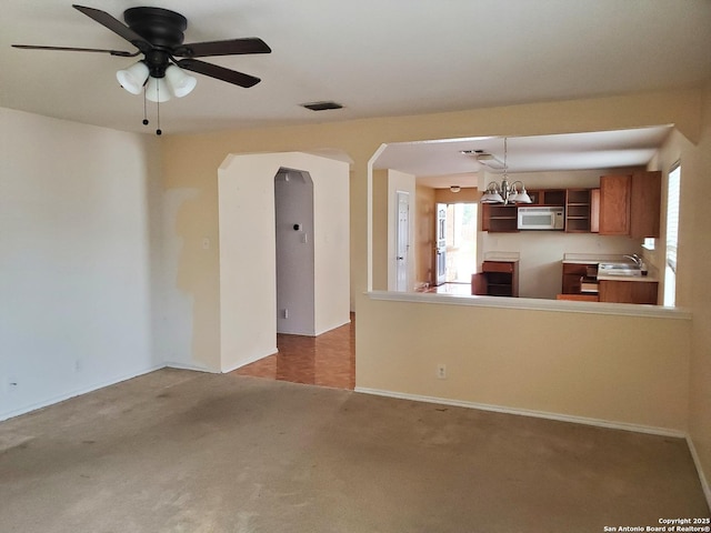 unfurnished living room with arched walkways, ceiling fan with notable chandelier, a sink, carpet flooring, and visible vents