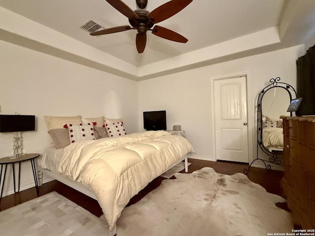 bedroom featuring baseboards, visible vents, a raised ceiling, and wood finished floors