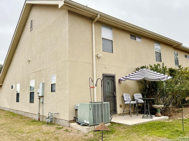 back of house featuring a patio area, stucco siding, a lawn, and central air condition unit