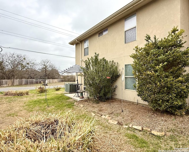 view of side of home featuring central AC unit, stucco siding, fence, and a yard