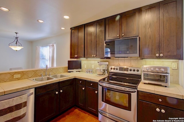 kitchen featuring tile countertops, stainless steel appliances, tasteful backsplash, a sink, and dark brown cabinets