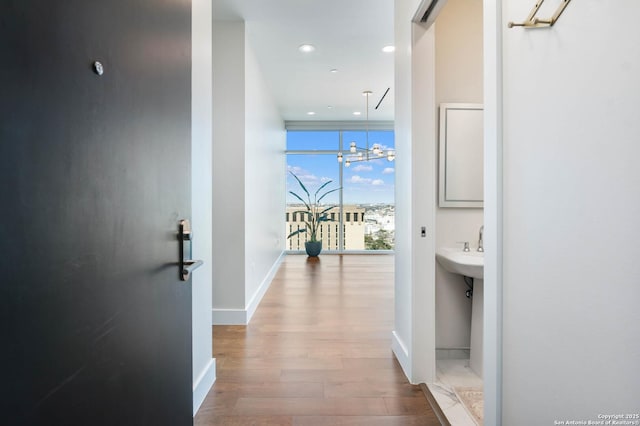 hallway with a notable chandelier, recessed lighting, wood finished floors, a wall of windows, and baseboards