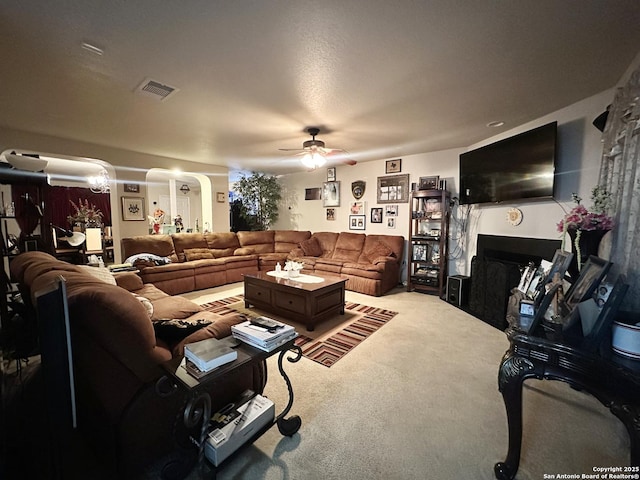 carpeted living area featuring arched walkways, ceiling fan, a fireplace, and visible vents