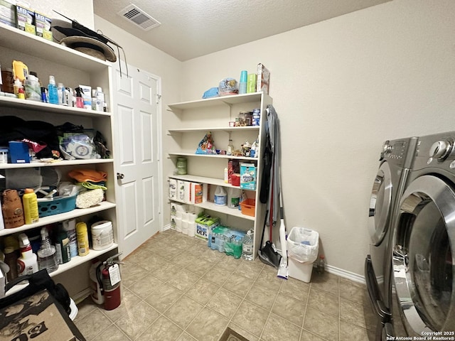 clothes washing area with visible vents, a textured ceiling, washer and dryer, laundry area, and baseboards