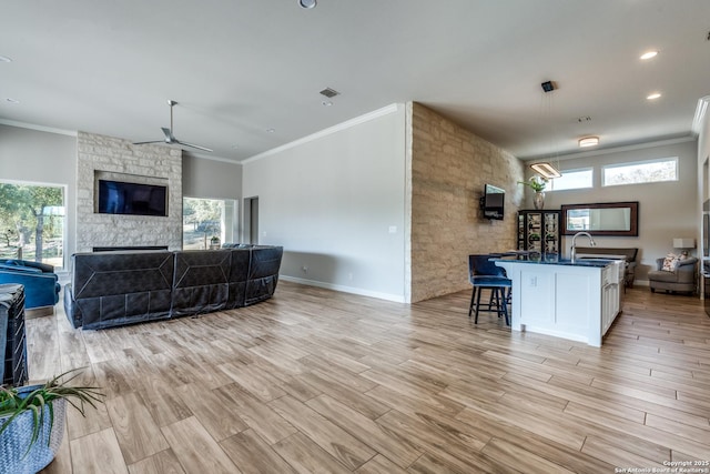 living room featuring light wood-style flooring, visible vents, a wealth of natural light, and a stone fireplace