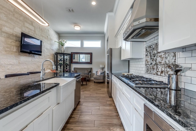 kitchen featuring tasteful backsplash, white cabinets, extractor fan, crown molding, and a sink