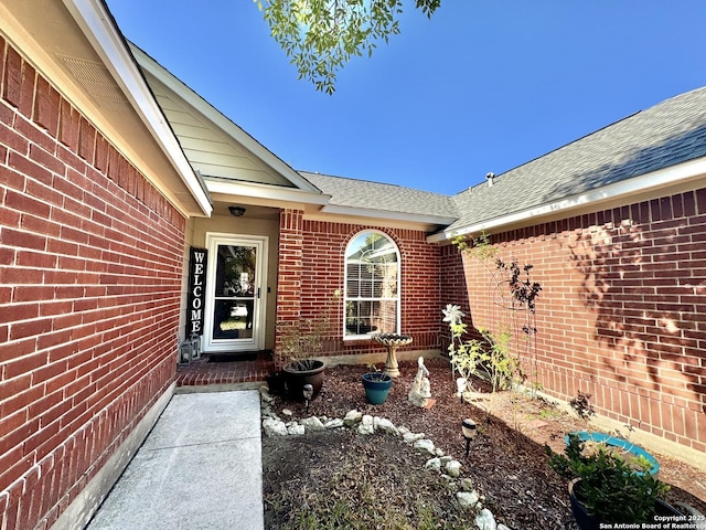 doorway to property featuring brick siding and roof with shingles