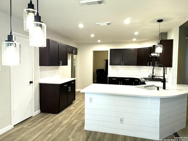 kitchen featuring a peninsula, light wood-style flooring, visible vents, and a sink