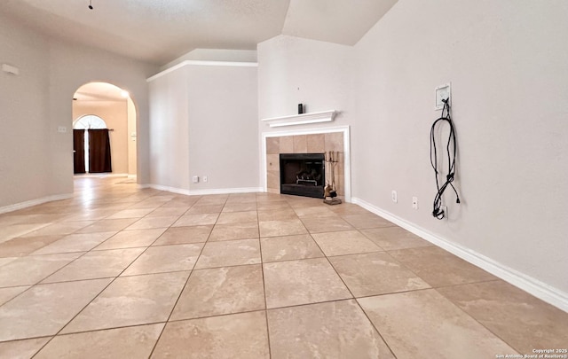 unfurnished living room with tile patterned floors, arched walkways, baseboards, and a tile fireplace