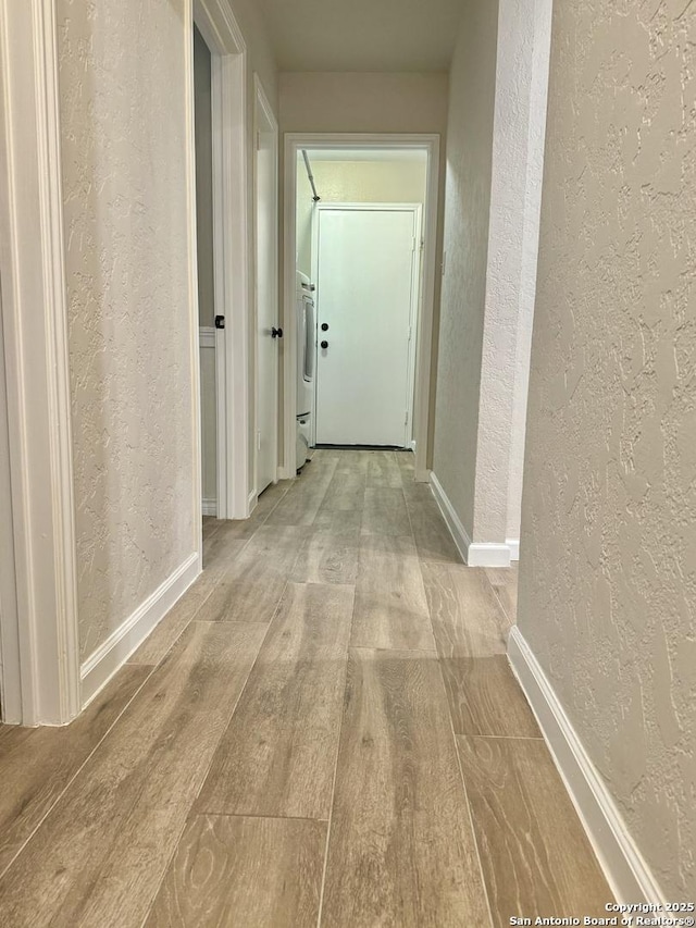 hallway with wood finished floors, a textured wall, baseboards, and washer / dryer