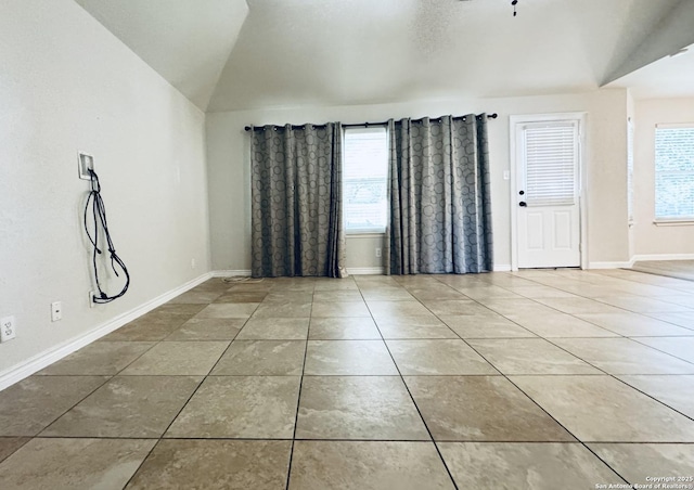 tiled empty room featuring a wealth of natural light, baseboards, and vaulted ceiling