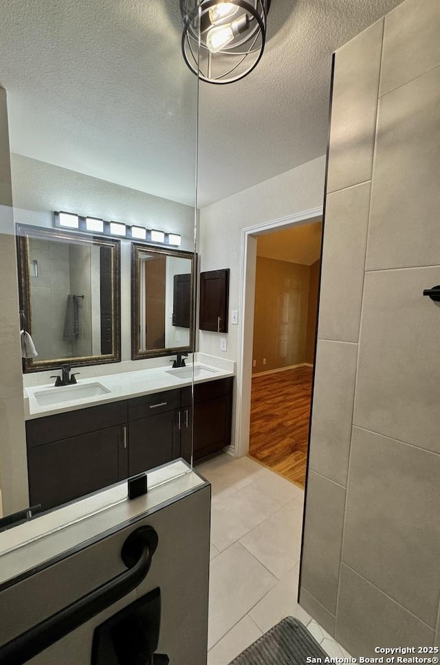 bathroom featuring a sink, a textured ceiling, double vanity, and tile patterned floors