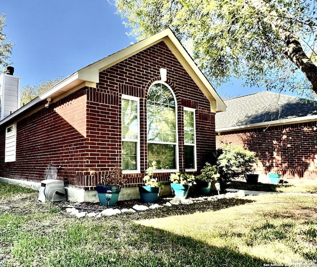 view of property exterior featuring brick siding, roof with shingles, and a chimney