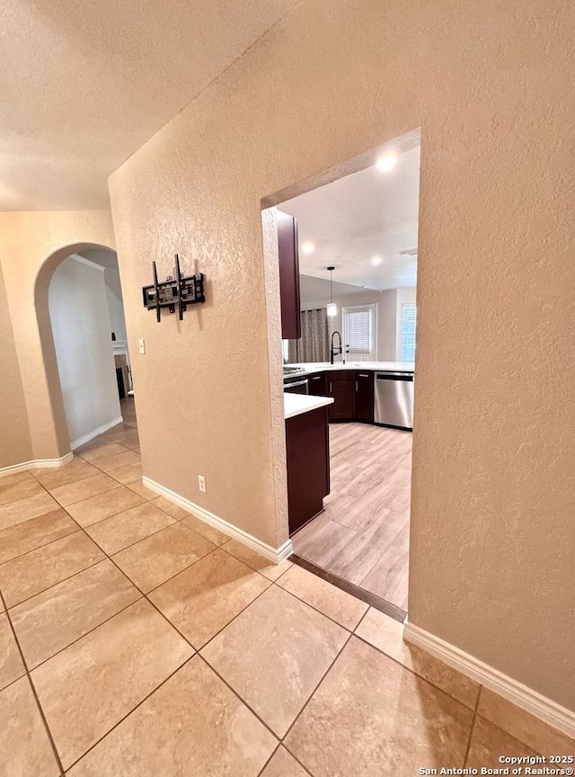 hall featuring light tile patterned floors, baseboards, and a textured wall