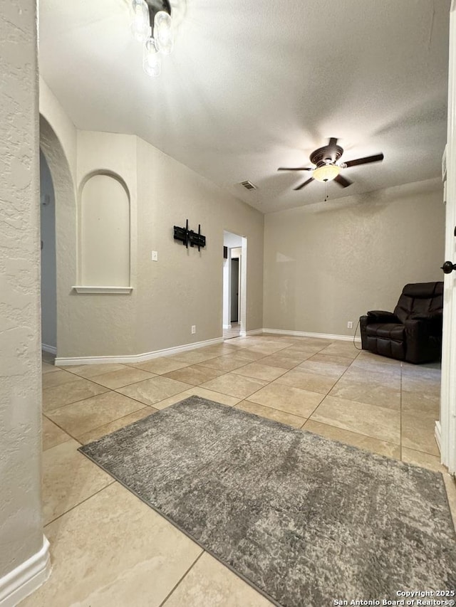 living area with visible vents, a textured wall, arched walkways, a textured ceiling, and a ceiling fan