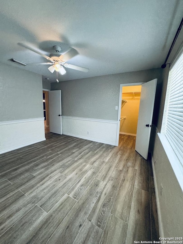 empty room with visible vents, a textured ceiling, wood finished floors, and a ceiling fan