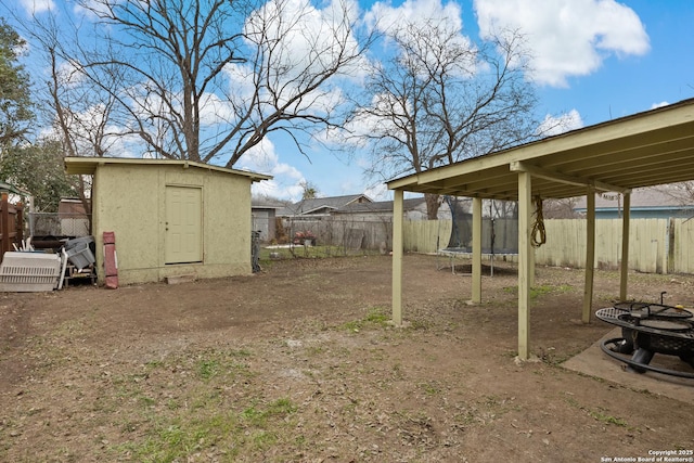 view of yard featuring a fenced backyard, a fire pit, an outdoor structure, a storage unit, and a trampoline