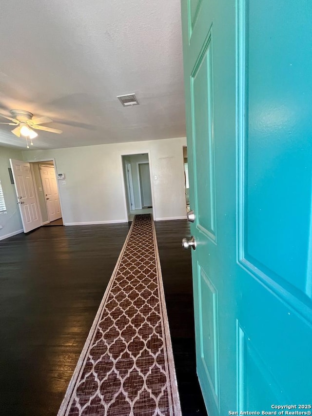 hall with baseboards, visible vents, and dark wood-type flooring