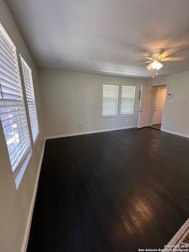 unfurnished room with a ceiling fan, baseboards, and dark wood-style flooring