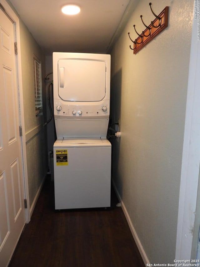 clothes washing area with dark wood-style floors, laundry area, baseboards, and stacked washing maching and dryer