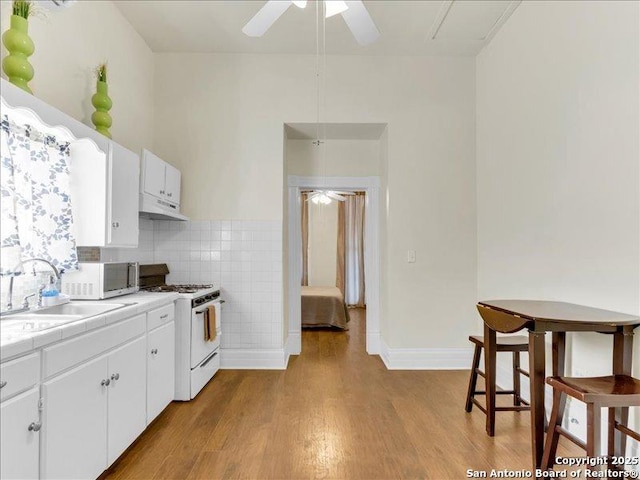 kitchen with tile counters, wood finished floors, gas range gas stove, under cabinet range hood, and a sink