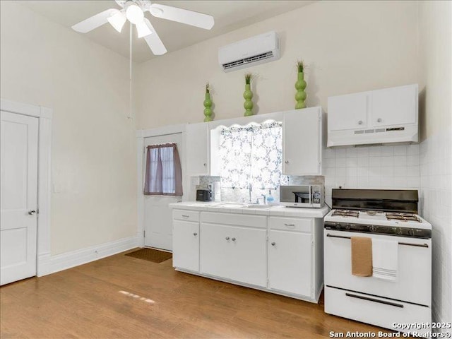 kitchen with decorative backsplash, white cabinets, white range with gas cooktop, a wall mounted air conditioner, and under cabinet range hood