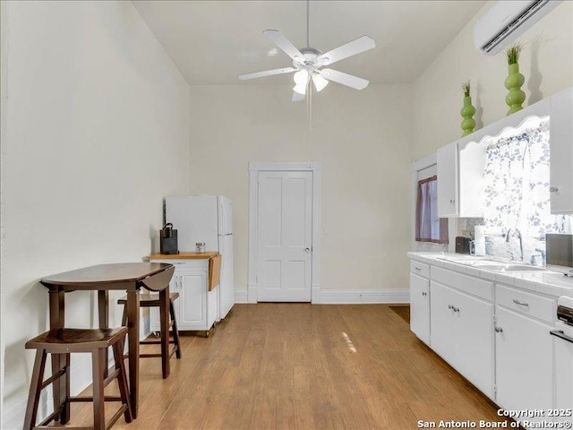 kitchen with light wood-style flooring, white cabinetry, a sink, and a wall mounted air conditioner