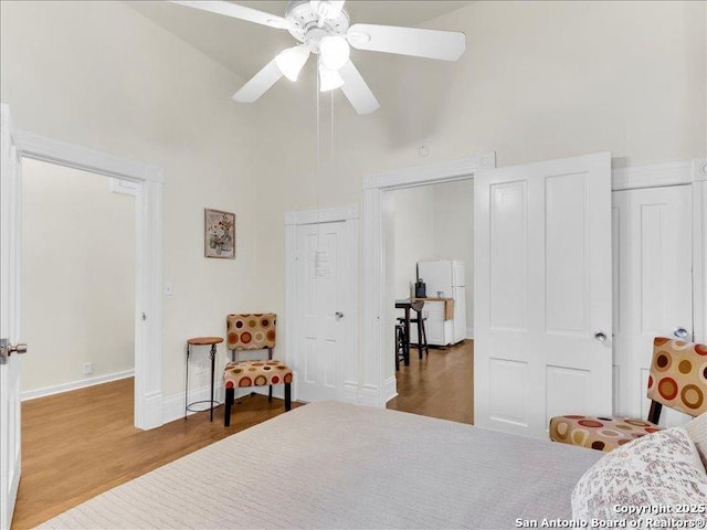 bedroom with ceiling fan, high vaulted ceiling, wood finished floors, baseboards, and freestanding refrigerator