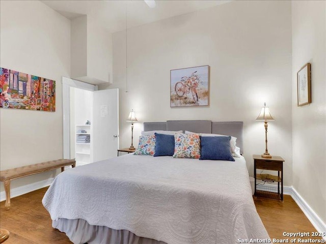 bedroom with wood finished floors, a towering ceiling, and baseboards