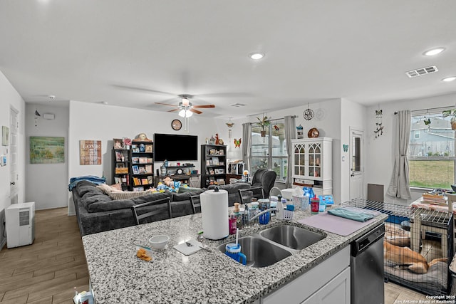 kitchen with light wood finished floors, visible vents, a kitchen island with sink, a sink, and dishwasher