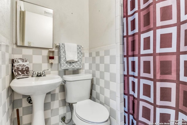 bathroom featuring toilet, a wainscoted wall, tile walls, and a shower with curtain