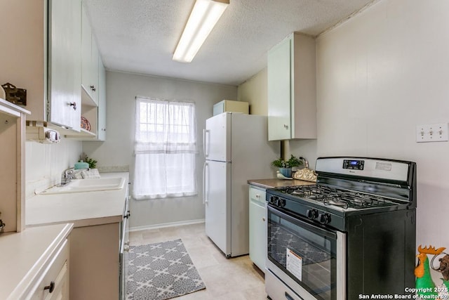 kitchen with gas range, freestanding refrigerator, light countertops, a textured ceiling, and a sink