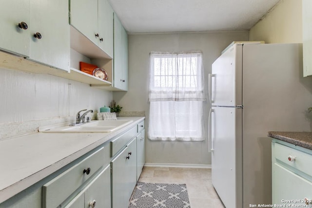 kitchen with baseboards, open shelves, a sink, and freestanding refrigerator