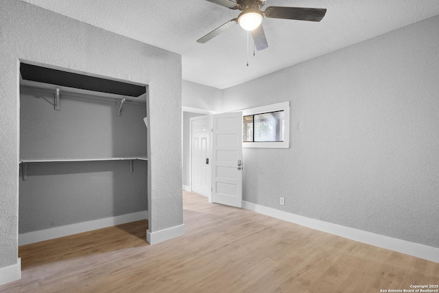 unfurnished bedroom featuring a textured ceiling, a textured wall, wood finished floors, baseboards, and a closet