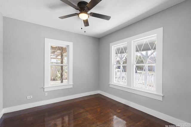 spare room featuring baseboards, dark wood-style flooring, a ceiling fan, and a healthy amount of sunlight