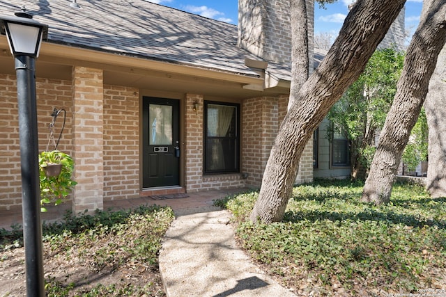 entrance to property featuring roof with shingles and brick siding