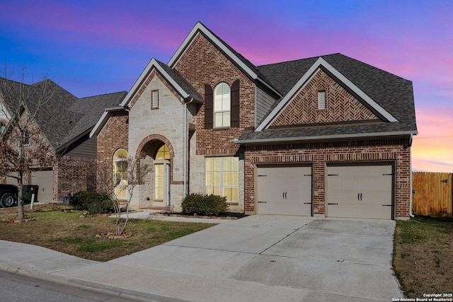 french country style house with stone siding, brick siding, concrete driveway, and roof with shingles