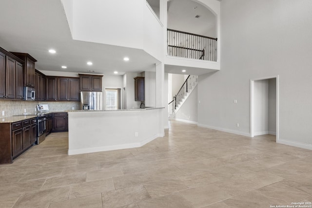 kitchen with decorative backsplash, appliances with stainless steel finishes, dark brown cabinets, light stone countertops, and baseboards