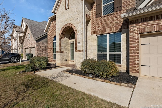 property entrance featuring a garage, stone siding, brick siding, and a yard