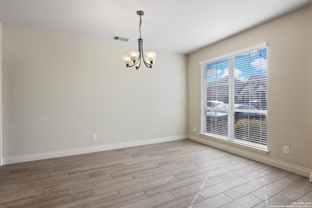 empty room with a chandelier, light wood finished floors, visible vents, and baseboards