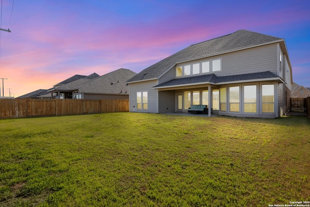 rear view of property with a fenced backyard, a shingled roof, a lawn, and a patio