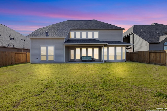 rear view of house featuring a yard, a shingled roof, a patio, and a fenced backyard