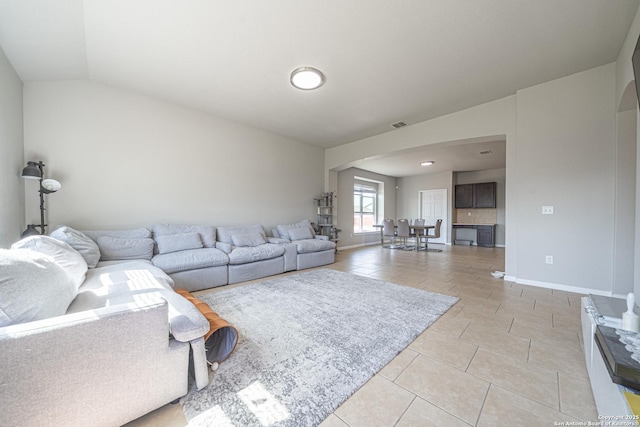 living area featuring light tile patterned floors, arched walkways, lofted ceiling, visible vents, and baseboards